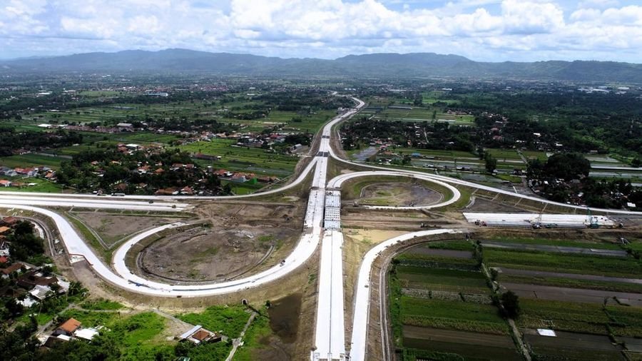 Pembangunan simpang susun Jalan Tol Solo–Yogyakarta–Kulonprogo dilihat dari udara, menunjukkan progres fisik konstruksi di tengah area persawahan.